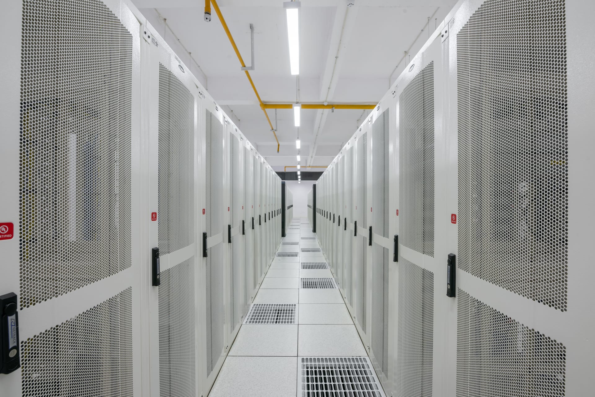 A brightly lit modern data center corridor, rows of white server racks stretching into the distance.